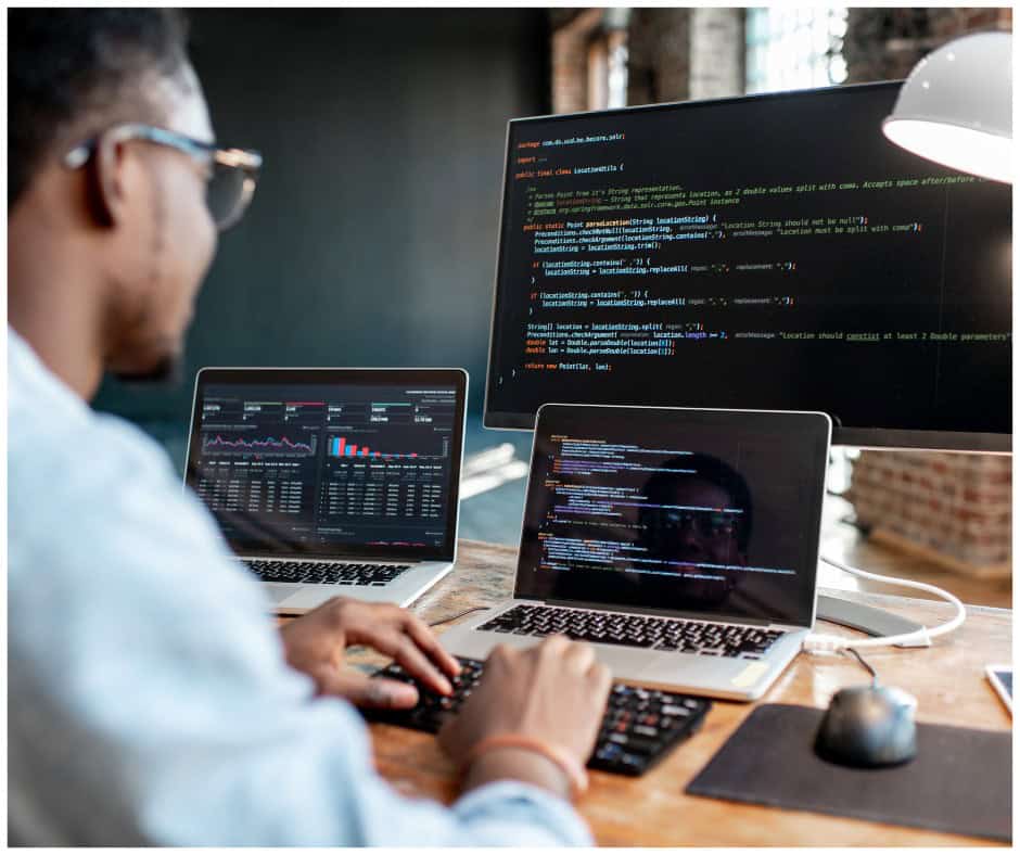 male student coding on multiple computer screens