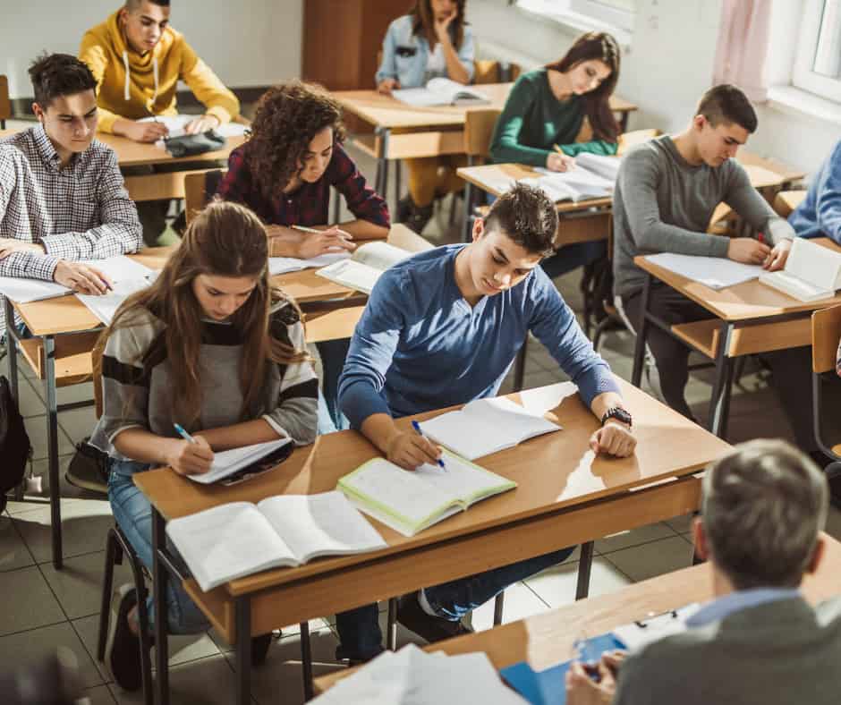 High school students studying in class with teacher at his desk